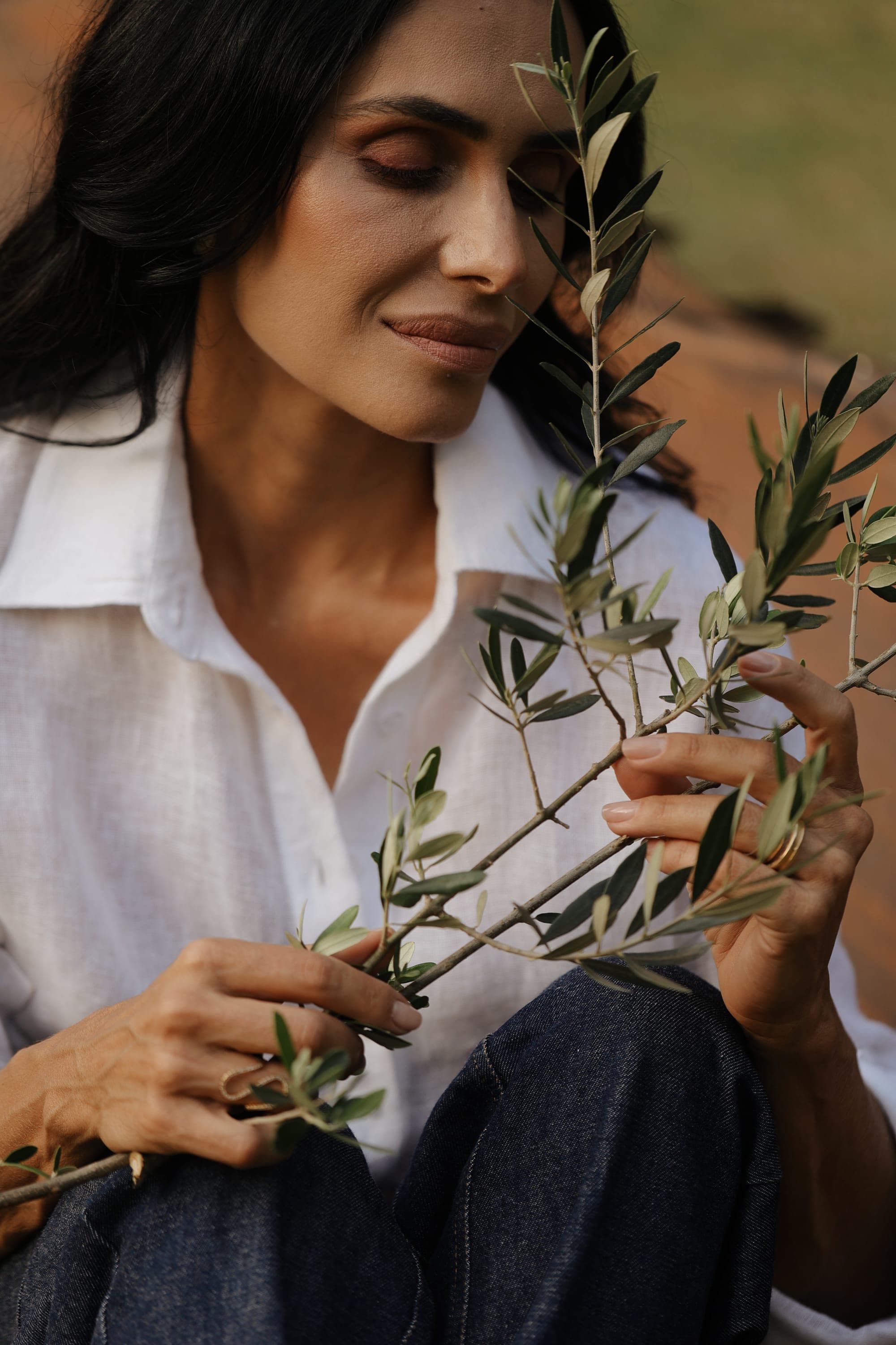 Mulher sorrindo em meio à natureza, segurando um ramo de oliveira