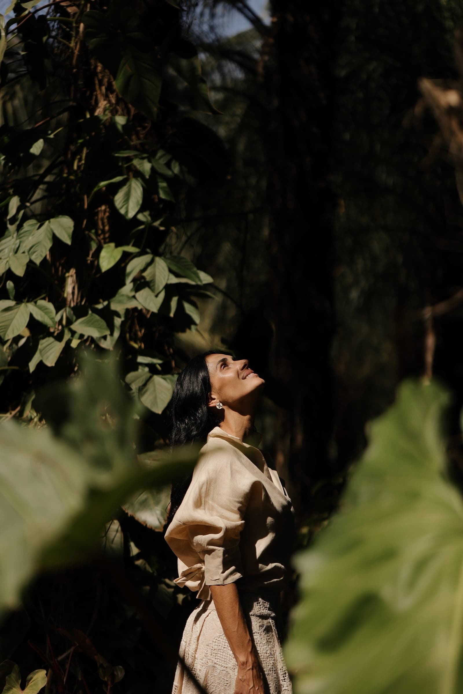 Mulher em vestido verde-oliva na floresta, rosto voltado para a luz entre as folhas